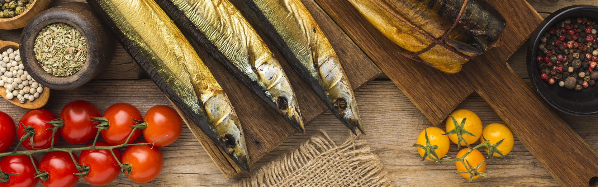 Goldbraun geräucherter Fisch, dazu frische Tomaten, Gewürze und Pfefferkörner, stilvoll auf einem rustikalen Holzbrett präsentiert.