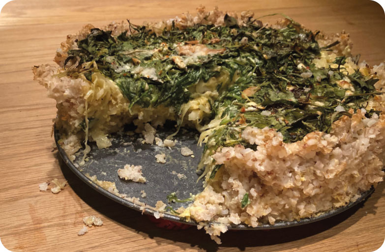 Kräuterkuchen_Rezept_Mai_1 Zutaten für Giouvetsi mit Orzo-Nudeln in einer Küche vorbereitet: gewürfeltes rohes Fleisch auf einem Brett, daneben Teller mit geschnittenem Lauch, Karotten und Sellerie, ein Topf und Bräter auf dem Herd, rote Küchenaccessoires im Hintergrund