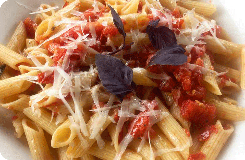 Pasta-mit-Tomaten-sugo_Pasta-Teller Ein Teller mit Penne-Pasta, garniert mit frischer Tomatensauce, geriebenem Parmesan und violettem Basilikum.